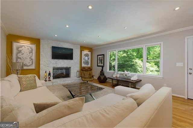 living area with crown molding, wood finished floors, a stone fireplace, recessed lighting, and baseboards
