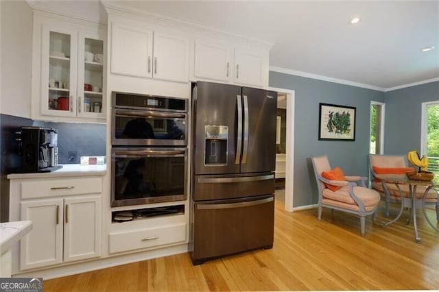 kitchen featuring stainless steel appliances, light wood-style flooring, white cabinetry, light countertops, and glass insert cabinets