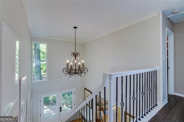 hallway with an upstairs landing, healthy amount of natural light, wood finished floors, ornamental molding, and a chandelier