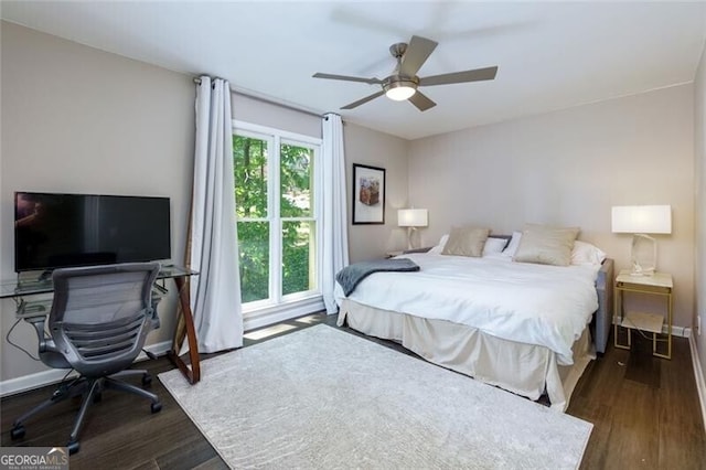 bedroom with wood finished floors, an office area, a ceiling fan, and baseboards