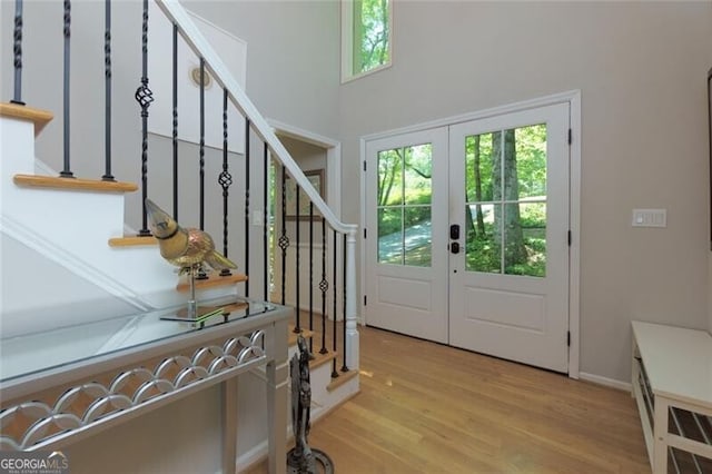 foyer entrance featuring stairway, wood finished floors, french doors, a towering ceiling, and baseboards