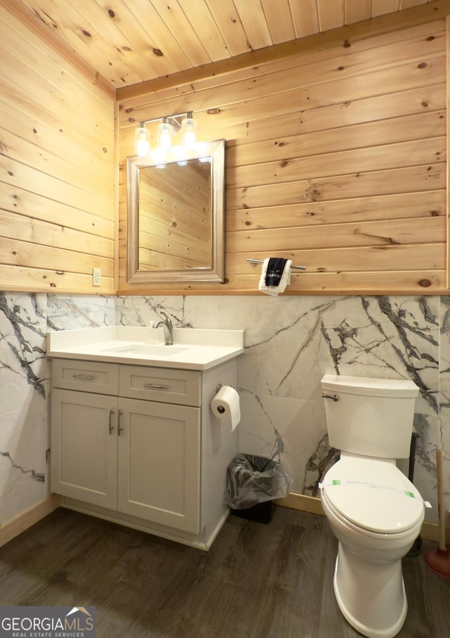 half bathroom featuring wood finished floors, vanity, toilet, wooden walls, and wood ceiling