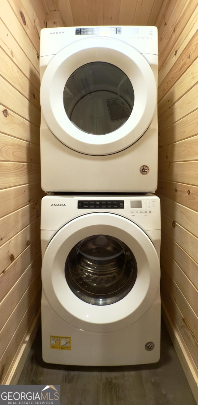 clothes washing area with estacked washer and dryer and wood walls