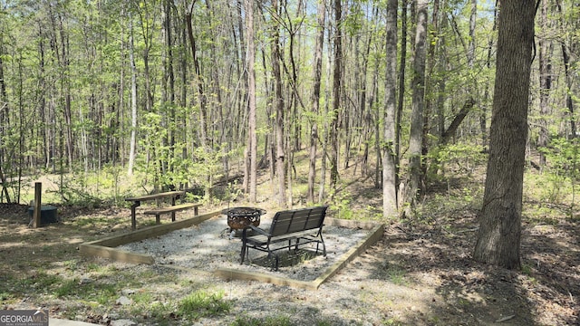 view of yard featuring an outdoor fire pit and a wooded view