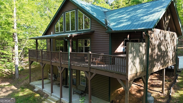 back of property featuring faux log siding, a wooden deck, a patio, and metal roof