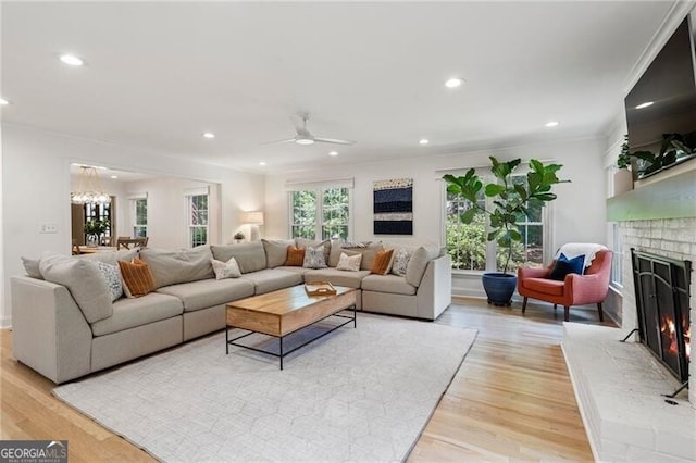 living area featuring a brick fireplace, crown molding, a chandelier, light wood-style floors, and recessed lighting