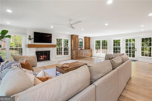 living area featuring a lit fireplace, a ceiling fan, recessed lighting, and light wood finished floors