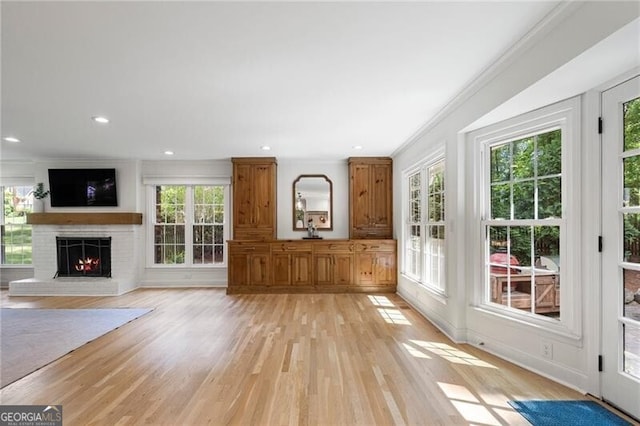 unfurnished living room featuring plenty of natural light, a brick fireplace, light wood-style flooring, crown molding, and recessed lighting