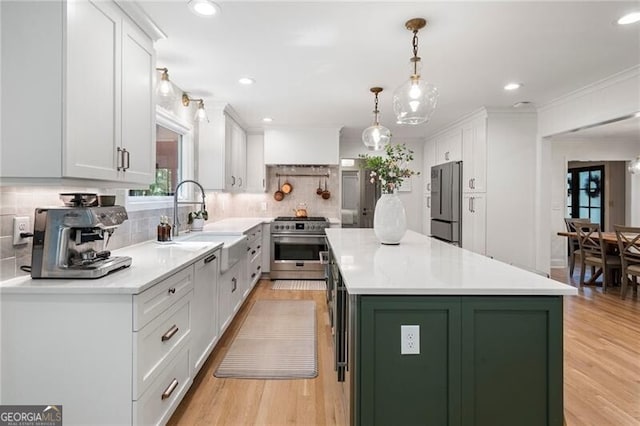 kitchen with appliances with stainless steel finishes, green cabinetry, white cabinetry, a sink, and light wood-style floors
