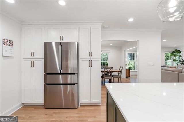 kitchen with freestanding refrigerator, light stone counters, crown molding, white cabinetry, and light wood-style flooring