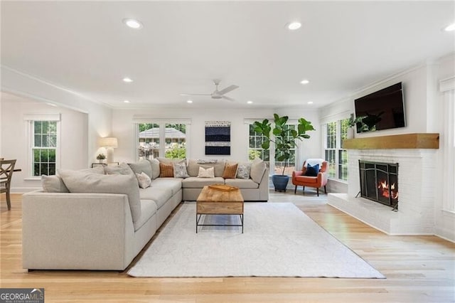 living room featuring a fireplace, a ceiling fan, light wood-type flooring, recessed lighting, and crown molding