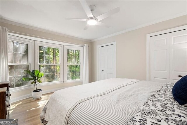 bedroom with two closets, crown molding, wood finished floors, a ceiling fan, and baseboards