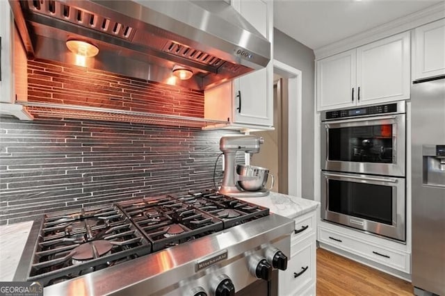 kitchen featuring stainless steel appliances, tasteful backsplash, wall chimney range hood, and white cabinets