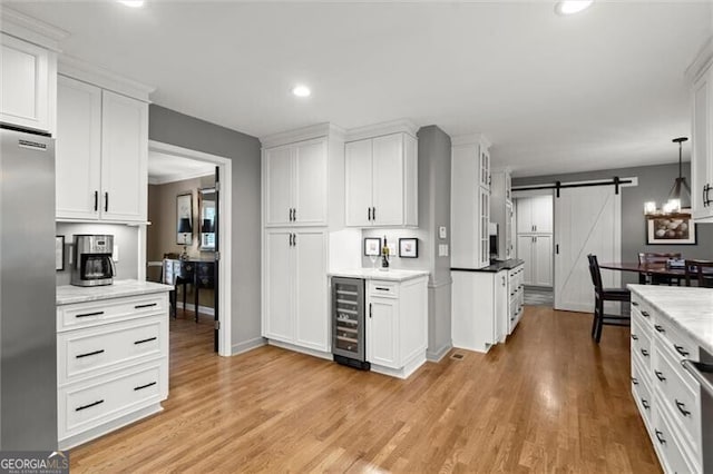 kitchen featuring beverage cooler, stainless steel built in fridge, a barn door, white cabinetry, and light wood-style flooring