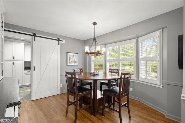 dining space with light wood finished floors, a barn door, a chandelier, and baseboards