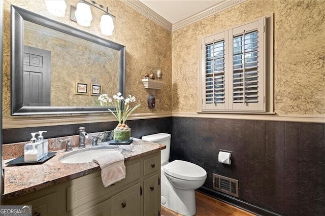 half bath featuring crown molding, wainscoting, wallpapered walls, wood finished floors, and toilet