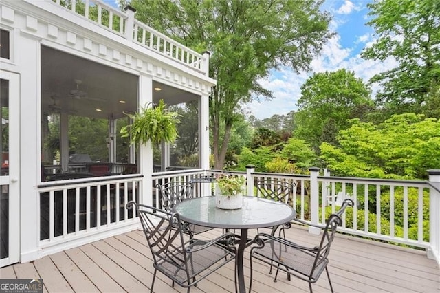 wooden terrace with a sunroom, outdoor dining space, and view of scattered trees