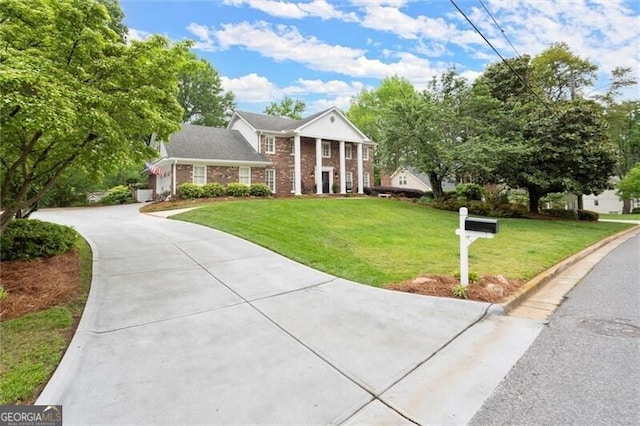 neoclassical home featuring brick siding, driveway, and a front yard