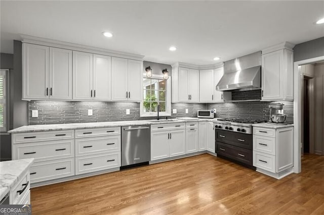 kitchen with stainless steel appliances, wall chimney exhaust hood, white cabinetry, backsplash, and recessed lighting