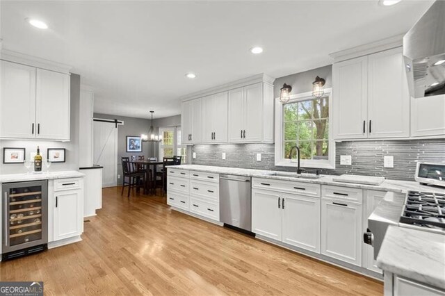 kitchen featuring a sink, beverage cooler, stainless steel dishwasher, a barn door, and white cabinetry