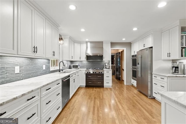 kitchen featuring stainless steel appliances, wall chimney range hood, a sink, white cabinets, and recessed lighting