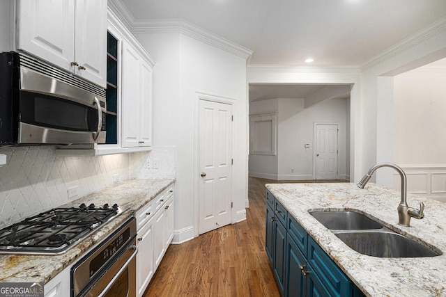 kitchen with appliances with stainless steel finishes, blue cabinets, a sink, white cabinetry, and wood finished floors