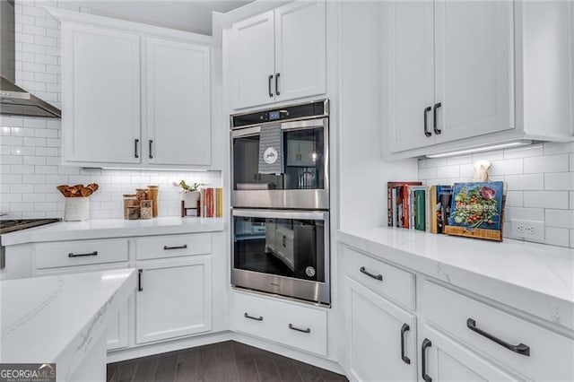 6150 Bridge Fair Rd, Cumming, GA 30028 - kitchen featuring stainless steel double oven, wall chimney range hood, white cabinetry, and backsplash