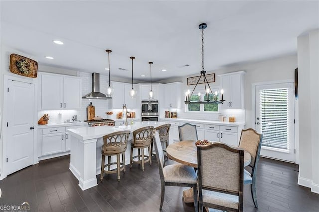 6150 Bridge Fair Rd, Cumming, GA 30028 - kitchen with wall chimney range hood, double oven, light countertops, backsplash, and an island with sink