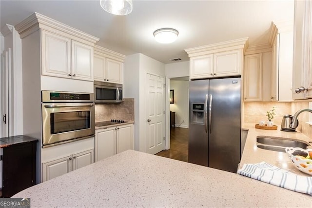 kitchen featuring appliances with stainless steel finishes, a sink, backsplash, and light stone counters