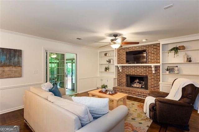 living area featuring ornamental molding, wood finished floors, a ceiling fan, a fireplace, and built in features