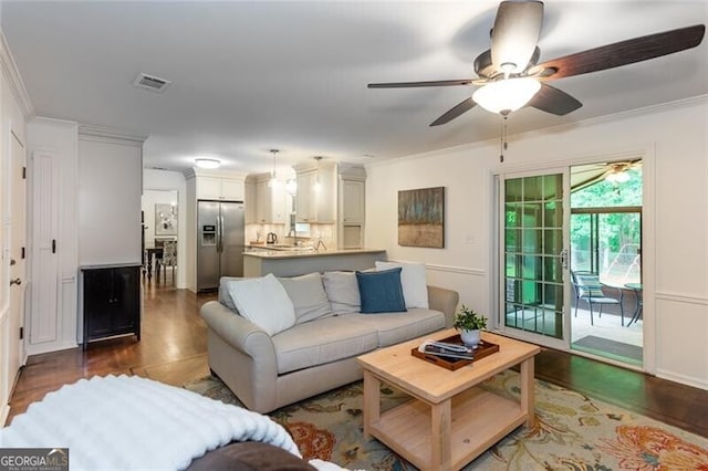 living room featuring dark wood-style flooring, crown molding, and a ceiling fan