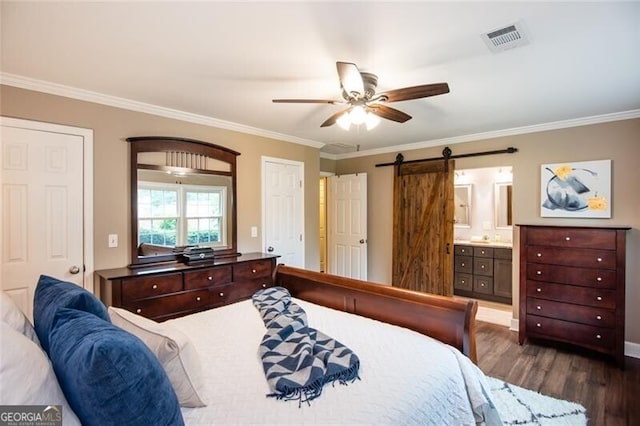 bedroom featuring a barn door, crown molding, dark wood-type flooring, ensuite bathroom, and ceiling fan