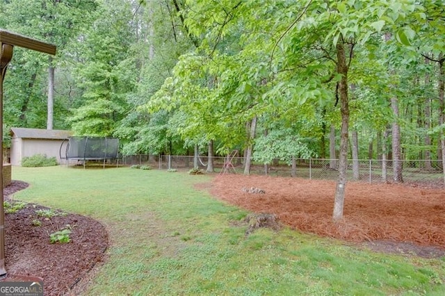 view of yard featuring a trampoline, an outbuilding, a wooded view, and a shed