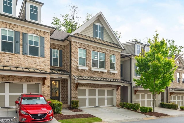 townhome / multi-family property with a standing seam roof, driveway, a garage, metal roof, and brick siding