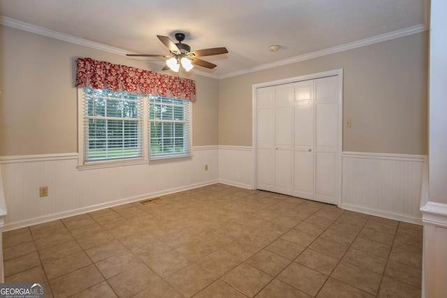 unfurnished bedroom with a wainscoted wall, ornamental molding, a closet, and ceiling fan