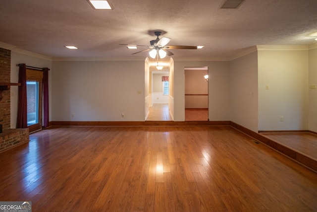 empty room featuring wood finished floors, baseboards, ceiling fan, ornamental molding, and a fireplace