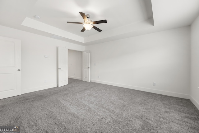spare room with a raised ceiling, ceiling fan, carpet, and baseboards