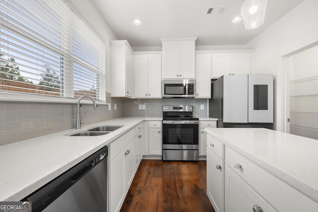 kitchen featuring appliances with stainless steel finishes, a sink, decorative backsplash, white cabinetry, and dark wood-type flooring