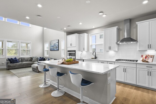 2436 Hidden Creek Rd, Kennesaw, GA 30152 - kitchen with wall chimney exhaust hood, a breakfast bar area, open floor plan, a kitchen island, and white cabinets