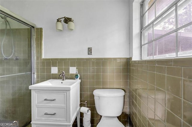 bathroom featuring tile walls, healthy amount of natural light, vanity, tiled shower, and toilet