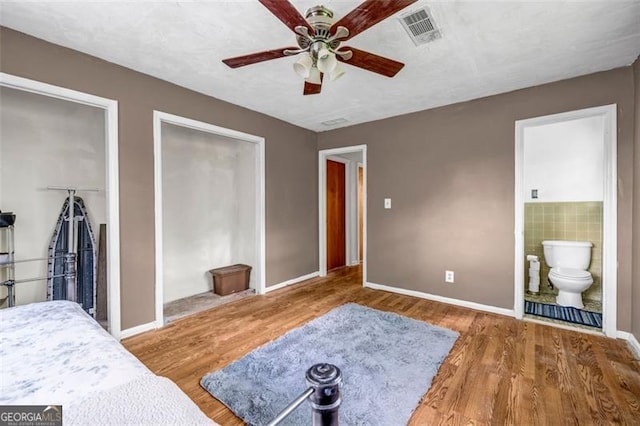 bedroom featuring multiple closets, wood finished floors, baseboards, ensuite bathroom, and a ceiling fan