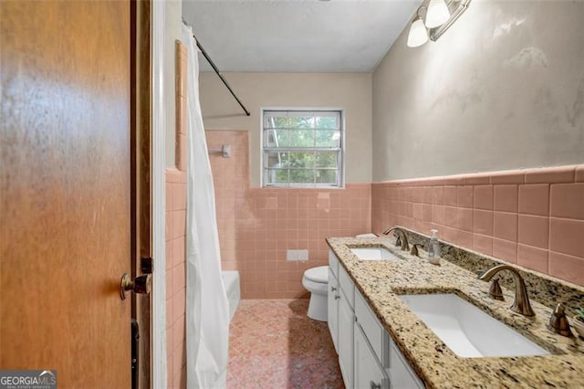 full bath with toilet, tile walls, double vanity, wainscoting, and shower / tub combo