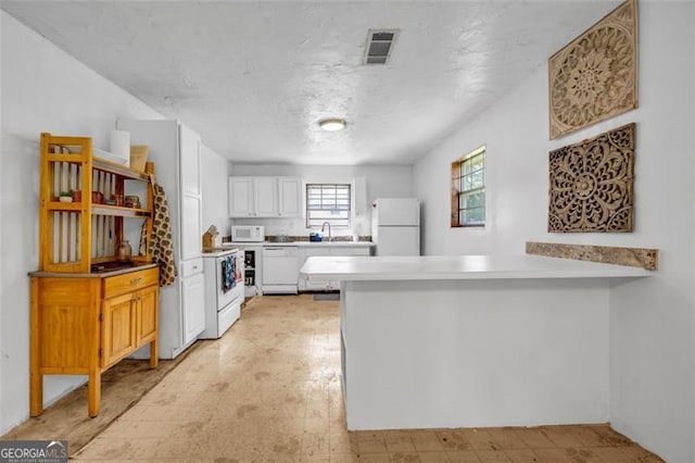 kitchen featuring white appliances, a peninsula, white cabinets, light countertops, and light floors