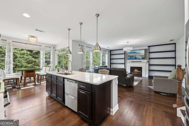 4630 Carriage Walk Ln, Cumming, GA 30040 - kitchen with stainless steel dishwasher, dark wood-type flooring, hanging light fixtures, an island with sink, and a warm lit fireplace