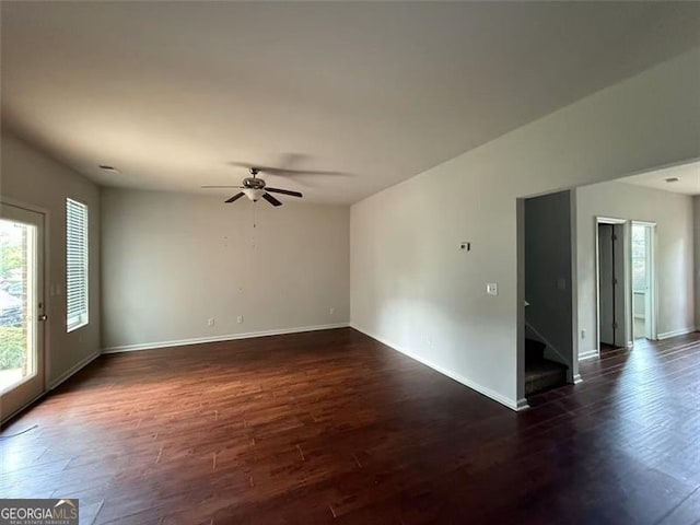 empty room featuring dark wood-style flooring, stairs, baseboards, and ceiling fan
