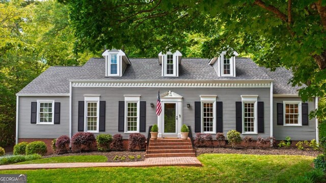 cape cod-style house featuring a front yard, a shingled roof, and a chimney