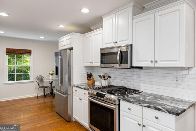 kitchen with appliances with stainless steel finishes, white cabinets, recessed lighting, dark stone countertops, and tasteful backsplash