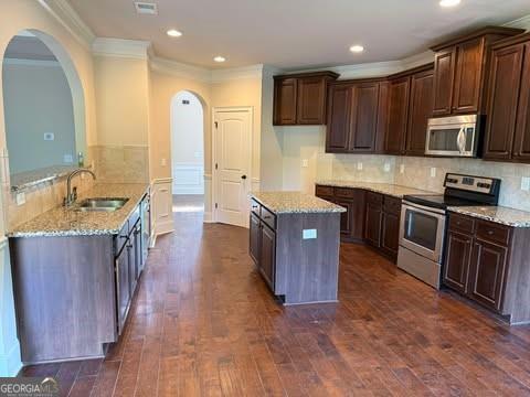1307 Clarecastle Ln, Buford, GA 30519 - kitchen with stainless steel appliances, a sink, ornamental molding, arched walkways, and light stone counters