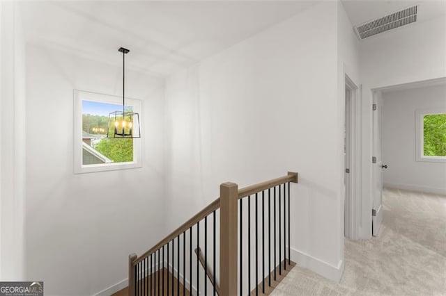 hall with an upstairs landing, a chandelier, carpet, and baseboards