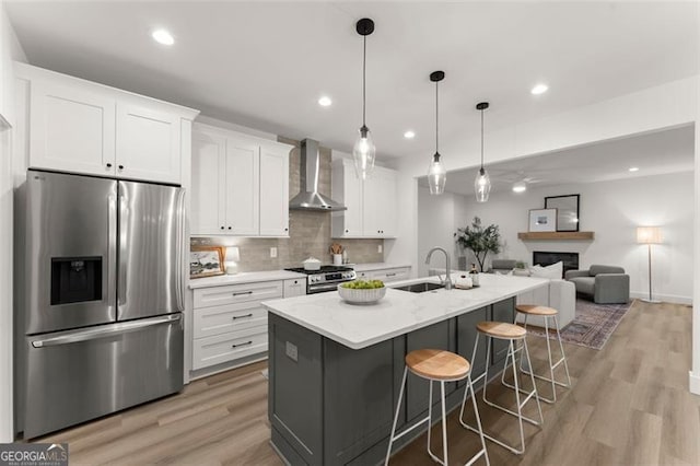 kitchen with stainless steel appliances, wall chimney exhaust hood, white cabinets, a sink, and light wood-type flooring